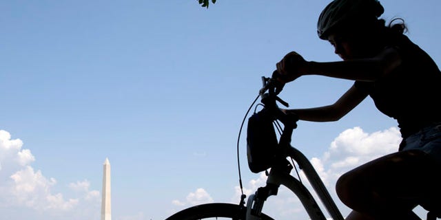 Aug. 17, 2015: A girl on a bicycle pedals around the Tidal Basin with the Washington Monument in the background.