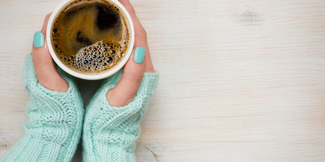 Female hands holding a coffee mug in knitted mittens
