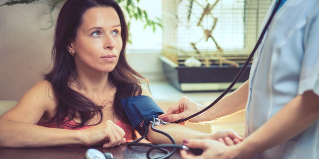 Beautiful young female doctor is checking the blood pressure of the patient.