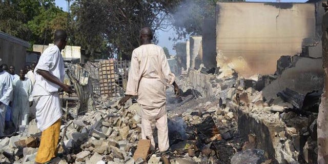 Residents watch as two men walk amidst rubble after Boko Haram militants raided the town of Benisheik in Nigeria. (Reuters)