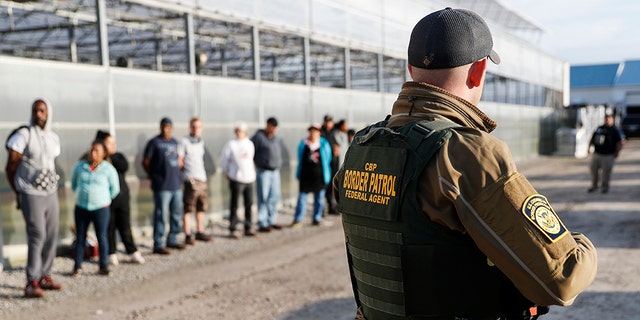 Immigration agents stand guard alongside suspects taken into custody during an immigration sting at Corso's Flower and Garden Center Tuesday in Castalia, Ohio.