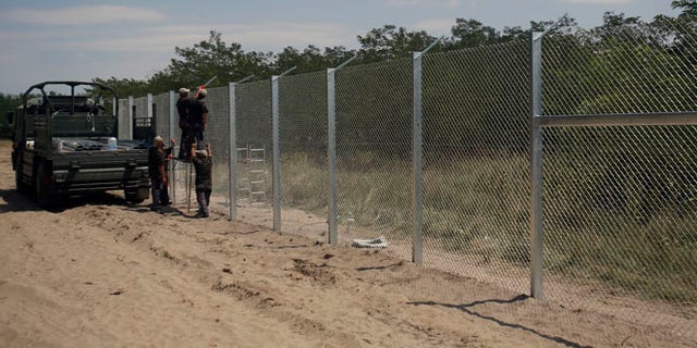 Hungarian soldiers build a fence near Morahalom, Hungary, Thursday, July 16, 2015. A fence on Hungary's border with Serbia to stem the flow of migrants and refugees will be complete by Nov. 30, the Hungarian defense minister said Thursday. Csaba Hende said that 900 people would work to install the fence, which is planned to be 4 meters (13 feet) high along the 175-kilometer (109-mile) border between Hungary and Serbia. (AP Photo/Darko Vojinovic)