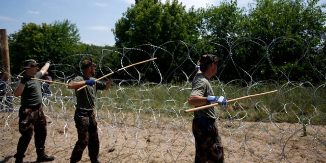 Hungarian soldiers place a barbed wire fence near Morahalom, Hungary, Thursday, July 16, 2015, as work continues to build a border fence between Hungary and Serbia to stem the flow of migrants. Defense Minister Csaba Hende said Thursday that 900 people would work simultaneously on 10-12 sections of the fence which is planned to be 4 meters (13 feet) high along the 175-kilometer (109-mile) border between Hungary and Serbia. (AP Photo/Darko Vojinovic)