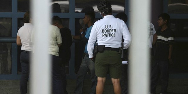 Illegal immigrants stand next to a Border Patrol agent before being deported from Arizona to the Mexican state of Sonora on July 26, 2010.