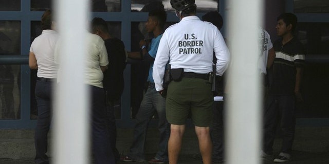 Illegal immigrants stand next to a Border Patrol agent before being deported from Arizona to the Mexican state of Sonora on July 26, 2010.