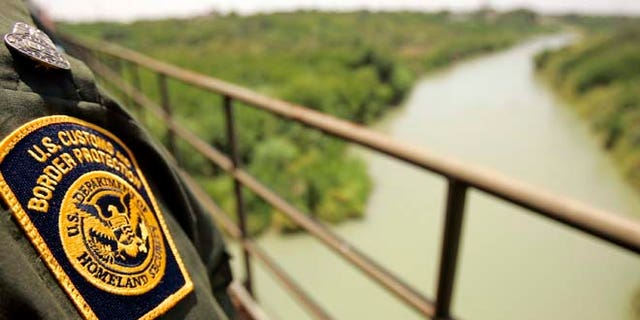 A Border Patrol agent looks over the Rio Grande with Mexico on the left and the U.S. on the right from a railroad bridge in Laredo.