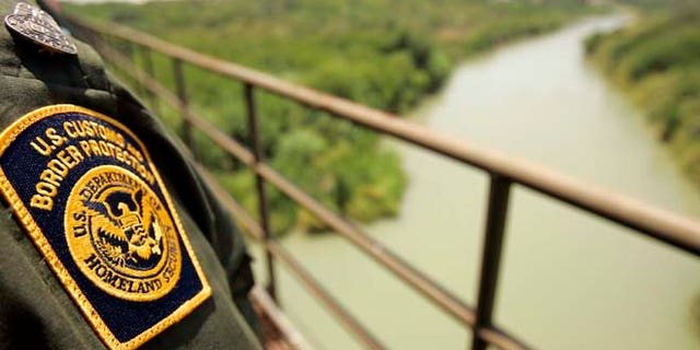 A Border Patrol agent looks over the Rio Grande with Mexico on the left and the U.S. on the right from a railroad bridge in Laredo.