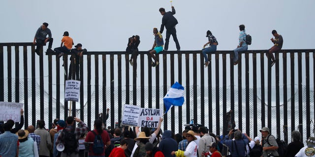 People climb the border wall fence as a caravan of migrants and supporters reached the United States-Mexico border near San Diego, California, U.S., April 29, 2018.