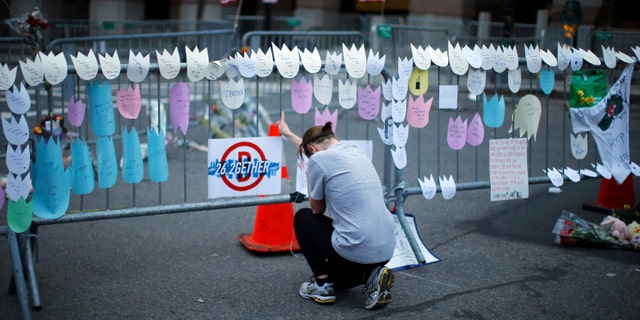 A woman kneels and cries in front of a memorial to the Boston Marathon bombings victims, at the barricades surrounding the scene in Boston, Massachusetts April 18, 2013.