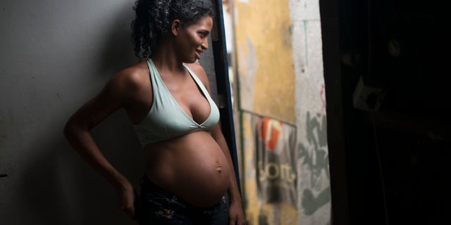 In this Jan. 29, 2016 photo, Tainara Lourenco smiles as she chats with neighbors from the entrance of home at a slum in Recife, Brazil. Unemployed and five months pregnant, 21-year-old Lourenco lives in a slum at the epicenter of Brazils tandem Zika and microcephaly outbreaks, the state of Pernambuco. (AP Photo/Felipe Dana)