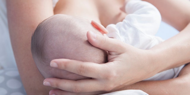 Mother holds her baby head while he is breastfed. Closeup