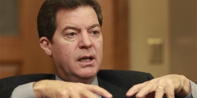 In this Dec. 21, 2010 photo, Kansas Gov. Sam Brownback is shown before taking office talking with a reporter in Topeka.