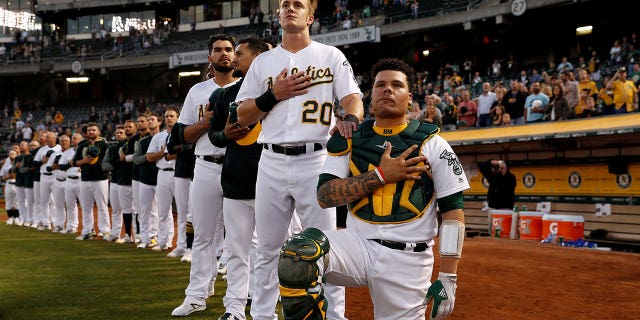 Bruce Maxwell of the Oakland Athletics kneels as teammate Mark Canha #20 places his hand on Maxwell's shoulder during the singing of the national anthem on September 25.