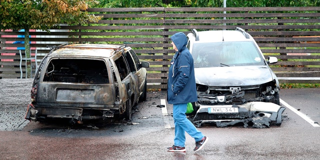 A person walks past burned cars parked at Frolunda Square in Gothenburg, Tuesday, Aug. 14, 2018. Masked youth torched dozens of cars overnight in Sweden and threw rocks at police, prompting an angry response from the prime minister, who on Tuesday spoke of an "extremely organized" night of vandalism. (Adam Ihse/TT via AP)