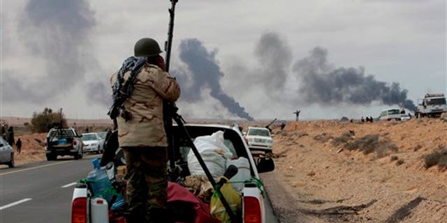 Anti-Libyan Leader Moammar Gadhafi rebel, stands behind his anti-aircraft machine gun as smokes rises from shell impacts in the distance during fighting against pro-Moammar Gadhafi forces, in Sedra, eastern Libya, on Wednesday March 9, 2011. Gadhafi appeared to be keeping up the momentum he has seized in recent days in his fight against rebels trying to move on the capital, Tripoli, from territory they hold in eastern Libya. (AP Photo/Hussein Malla)