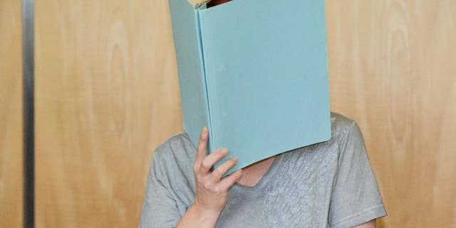 Defendant Andrea G., accused of murder, covering her face with a folder in the courtroom.