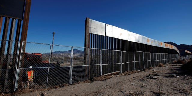 FILE: A worker stands next to a newly built section of the U.S.-Mexico border fence at Sunland Park, Calif.
