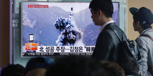 FILE - In this April 24, 2016 file photo, a man walks by as people watch a TV news program showing an image published earlier in the day in North Korea's Rodong Sinmun newspaper of North Korea's ballistic missile that the North claimed to have launched from underwater, at Seoul Railway station in Seoul, South Korea. With Donald Trump getting ready to become president, North Korea is talking about launching an ICBM and Washington officials are saying they will shoot down anything that threatens the territory of the U.S. or its allies. (AP Photo/Ahn Young-joon, File)