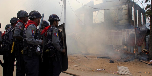 FILE - In this Thursday, March 21, 2013 file photo, armed Myanmar police officers provide security around a smoldering building following ethnic unrest between Buddhists and Muslims in Meikhtila, Mandalay division, about 550 kilometers (340 miles) north of Yangon, Myanmar. Few imagined Myanmar would embrace democracy when the U.S. began its historic engagement with the military regime. The country’s rapid changes were lauded by visiting Western leaders, and the nation’s president was hailed as a hero. But spasms of spreading, communal violence show the reform path is bumpier that expected and have taken the sheen off a foreign policy success of the Obama administration’s first term. (AP File Photo)