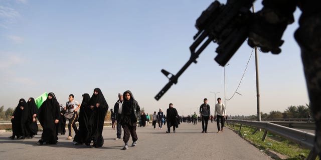 An Iraqi federal policeman stands guard as Shiite pilgrims march to Karbala for Arbaeen in Baghdad's southern district of Dora, Thursday, Dec. 19, 2013. The holiday marks the end of the 40-day mourning period after the anniversary of the 7th century martyrdom of Imam Hussein the Prophet Muhammad's grandson. A suicide bombing targeting Shiite pilgrims in Iraq's capital on their way to Karbala, a holy city, and other violence across the country killed more than 20 people Thursday, officials said. (AP Photo/Khalid Mohammed)