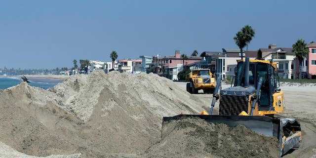 A bulldozer works to pile sand on a temporary berm to protect beach front homes on, Friday, Sept. 5, 2014, in Long Beach, Calif. Southern California is in for another round of high surf generated by what is currently Hurricane Norbert in the Pacific Ocean off Baja California. (AP Photo/Chris Carlson)