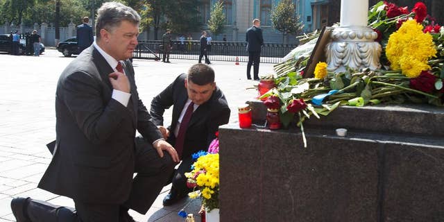Ukraine's President Petro Poroshenko, left, and parliament speaker Volodymyr Groisman lay flowers by the photo of a police officer who was killed in a Monday clash, in front of Parliament in Kiev, Ukraine, Tuesday, Sept. 1, 2015. Ukrainian police say 141 people remain hospitalized after a nationalist protest in Kiev turned violent, with 10 of the injured in serious condition. Two officers died from their wounds. (Anastasiia Sirotkina, Pool photo via AP)