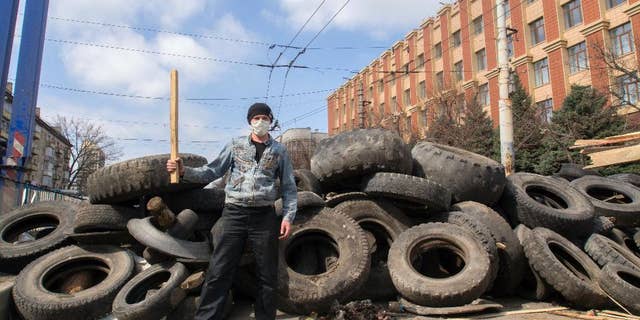 A masked pro-Russian activist poses for a photo in front of barricades at the Ukrainian regional office of the Security Service in Luhansk, 30 kilometers (20 miles) west of the Russian border, in Ukraine, Wednesday, April 9, 2014. Ukrainian Interior Minister Arsen Avakov said the standoff in Luhansk and the two neighboring Russian-leaning regions of Donetsk and Kharkiv must be resolved within two days.(AP Photo/Igor Golovniov)
