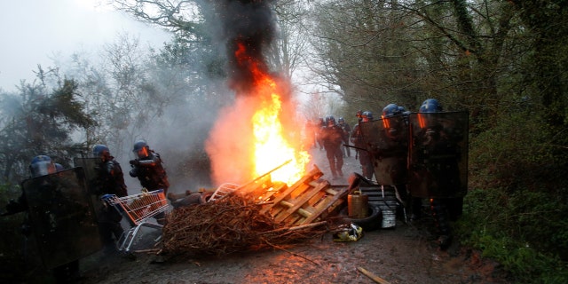French gendarmes stand near burning debris on a road during an evacuation operation in Notre-Dame-des-Landes, near Nantes, France.