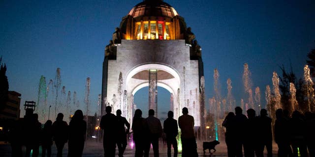 FILE - In this Dec. 26, 2012 file photo, pedestrians stand in front of the Arch of the Revolution monument in Mexico City. Moody's credit rating agency has changed the outlook for Mexico's debt rating from stable to negative, citing low oil prices and slow economic growth, according to a Moody's statement on Thursday, March 31, 2016. (AP Photo/Alexandre Meneghini, File)