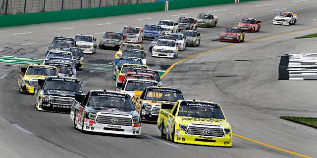 Pole-sitter Kyle Busch, right, leads the field into the first lap of the NASCAR Trucks auto race at Kentucky Speedway in Sparta, Ky., Thursday June 26, 2014. Darrell Wallace Jr. is at front left. (AP Photo/Garry Jones)