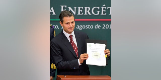 FILE - In this Aug. 12, 2013 file photo, Mexico's President Enrique Pena Nieto shows to the audience his proposal that would allow private firms to participate in the oil industry in Mexico City. The opening of Mexico's oil industry to private and foreign investment caps a remarkable series of legislative victories by President Pena Nieto, who is trying to re-engineer the country’s most dysfunctional institutions. (AP Photo/Eduardo Verdugo, File)