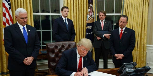 FILE - In this Jan. 20, 2017, file photo,President Donald Trump, flanked by Vice President Mike Pence and Chief of Staff Reince Priebus, signs his first executive order on health care in the Oval Office of the White House in Washington. (AP Photo/Evan Vucci, File)