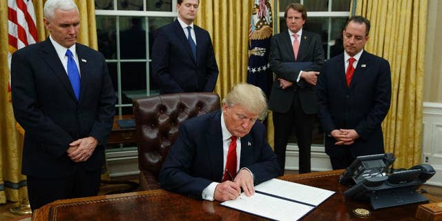 FILE - In this Jan. 20, 2017, file photo,President Donald Trump, flanked by Vice President Mike Pence and Chief of Staff Reince Priebus, signs his first executive order on health care in the Oval Office of the White House in Washington. (AP Photo/Evan Vucci, File)