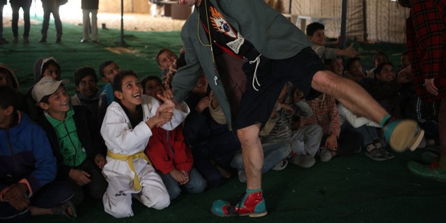 Moises Queralt, a clown from Mabsutins, a group of clowns from Spain, acts weak as a Syrian refugee child in a karate uniform pulls his arm during their show at Zaatari refugee camp near the Syrian border in Mafraq, Jordan, Sunday, Dec. 1, 2013. It was an unusual day for Syrian refugee children: Pinocchio and other show gigs live Sunday under a wind-swept tent in a sprawling desert camp straddling the Syrian border. (AP Photo/Mohammad Hannon)