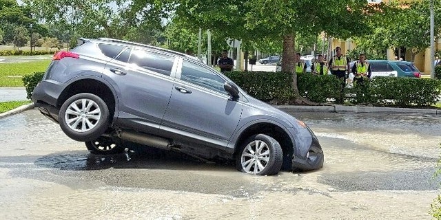This photo provided by Mike Jachles Broward Sheriff Fire Rescue shows a vehicle partially swallowed by a 10-foot-by-10-foot sinkhole on Thursday, July 7, 2016 in Cooper City, Fla. Dolores Otero drove toward the drive-thru and her car went nose-first into the water. One of the car's back tires was left hanging in the air. Otero and her grandson got safely out of the vehicle, which began to fill with water. (Mike Jachles/Broward Sheriff Fire Rescue via AP)