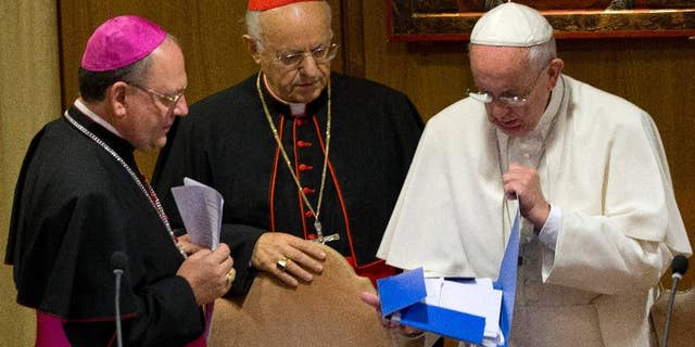 Pope Francis, right, checks a folder next to Bishop Fabio Fabene, left, and Cardinal Lorenzo Baldisseri as they arrive at a morning session of the two week-long Synod of bishops, at the Vatican, Tuesday, Oct. 6, 2015. (AP Photo/Alessandra Tarantino)
