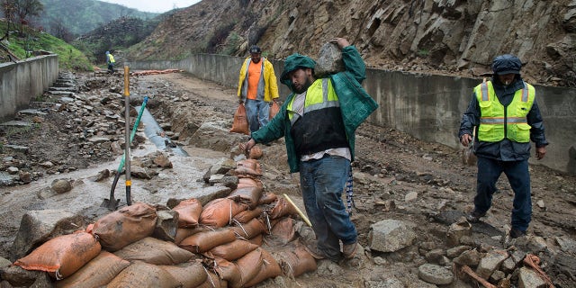 Workers place sandbags on a washed-out driveway on La Tuna Canyon Road in Sun Valley, Calif.
