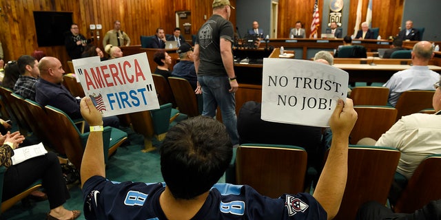 Jamie Park of Pico Rivera, Calif., holds up signs during a city council meeting at Pico Rivera City Hall on Tuesday.