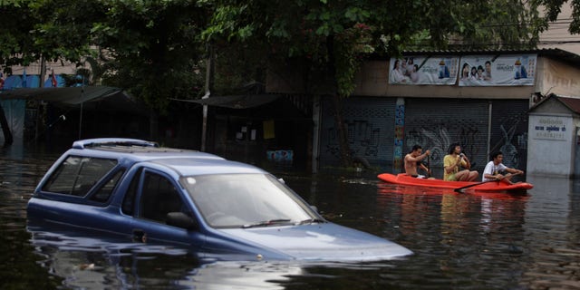 Oct. 28, 2011: Thai men row their boat past a vehicle submerged in floodwaters in Bangkok, Thailand.