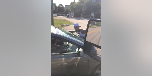 Video shows a woman clinging to the hood of a moving car, shouting for passersby to call the police.