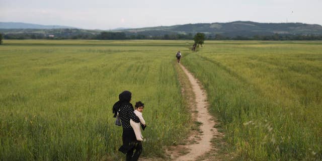 A woman walk with her baby on fields as a group of refugees and migrants leave the northern Greek border point of Idomeni, Greece, on Tuesday May 10, 2016. About 54,000 refugees and migrants are currently stranded in Greece as 10,000 are camped in Idomeni, after the European Union and Turkey reached a deal designed to stem the flow of refugees into Europe’s prosperous heartland. (AP Photo/Petros Giannakouris)