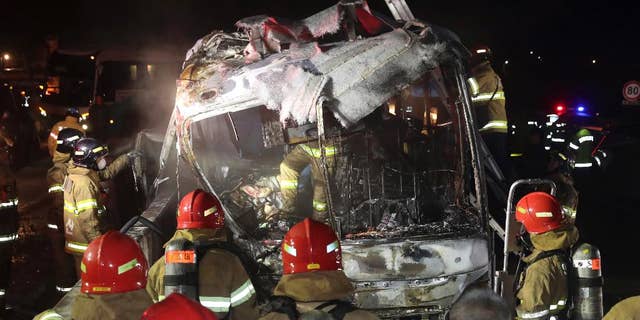 South Korean firefighters check a burned out bus on the Gyeongbu Expressway near the southeastern city of Ulsan, South Korea, Friday, Oct. 14, 2016. Twenty people, including the driver, were on the bus when it smashed into the guardrail and caught fire on the expressway, officials said. (Kim Yong-tae/Yonhap via AP) KOREA OUT