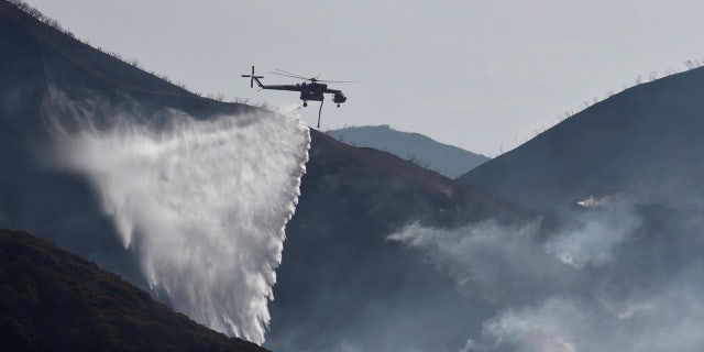 In this photo provided by the Santa Barbara County Fire Department, a Sikorsky S-64 Skycrane makes a water drop on hot spots along the hillside east of Gibraltar Road in Santa Barbara, Calif., Sunday morning, Dec. 17, 2017.