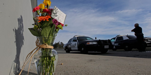 Flowers are left by the side of the road as a San Bernardino police officer blocks the road leading to the site of yesterday's mass shooting on Thursday, Dec. 3, 2015 in San Bernardino, Calif. A heavily armed man and woman dressed for battle opened fire on a holiday banquet for his co-workers Wednesday, killing multiple people and seriously wounding others in a precision assault, authorities said. Hours later, they died in a shootout with police. (AP Photo/Chris Carlson)