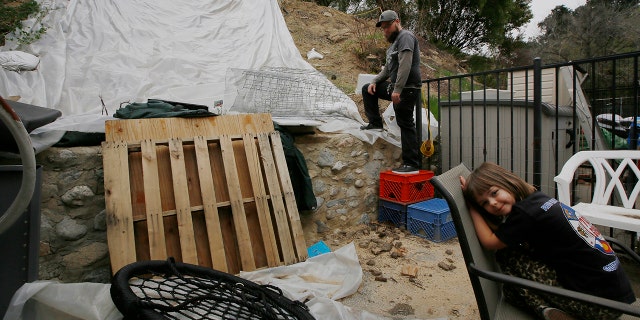 Andrew Joos-Visconti works to protect his back yard from the upcoming rains with a plastic tarp, in the Sun Valley area of Los Angeles Tuesday, March 20, 2018. At right, his daughter, Scarlett, 4.