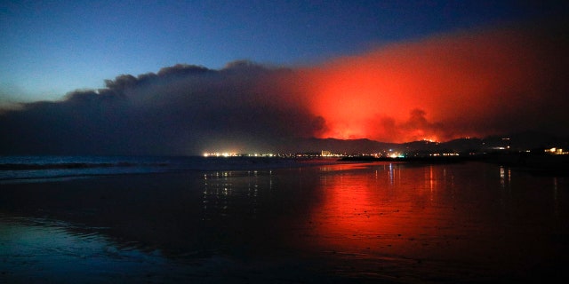 A wildfire continues to burn as its red glow is reflected on the beach on Tuesday.