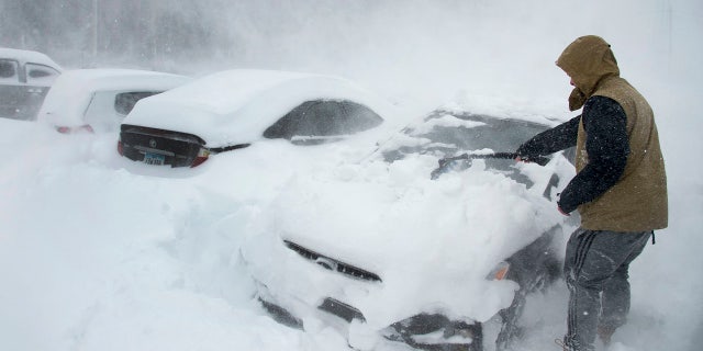 Heavy winds blow snow as Ryan Foster, 25, scrapes snow from his car in the parking lot where he lives at the Donner Summit Lodge in Norden on Thursday, March 1, 2018, near Donner Summit, Calif.