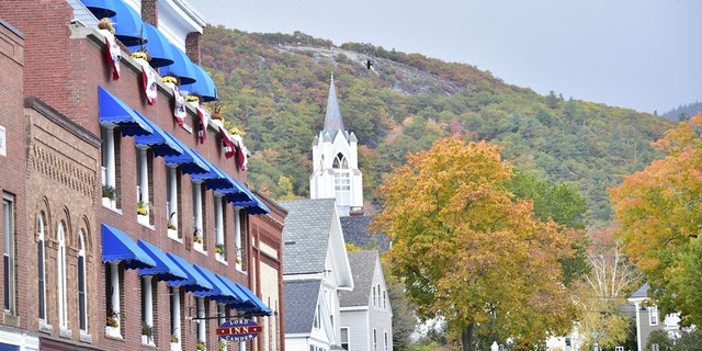 Camden, Maine, USA Bright blue awnings fill the streets of downtown while the steeple of the church is surrounded by Fall Foliage.