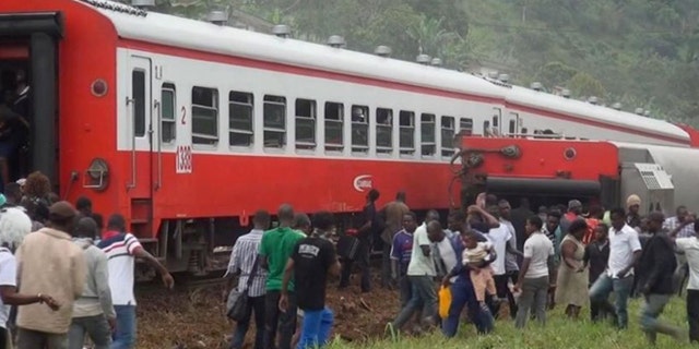 People walk beside a derailed train carriage after an accident in Eseka, Cameroon, Friday, Oct. 21, 2016. (Equinox TV via AP)