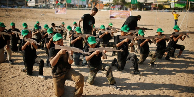 Palestinian boy Mahmoud Haniyeh (front, 1st L), 13, aims a wooden gun during a military-style exercise at a summer camp organized by the Hamas movement in Gaza City June 17, 2013. Tens of thousands of children from the Gaza Strip spend at least part of their holidays in special summer camps, arranged around a wide array of activities. Some, organised by the United Nations, offer sports, art and dance classes. Others, laid on by Gaza's Islamist rulers Hamas, include fun and games, while seeking to reinforce religious values and awareness of the conflict with Israel. Picture taken June 17, 2013. REUTERS/Mohammed Salem (GAZA - Tags: POLITICS EDUCATION SOCIETY)
ATTENTION EDITORS: PICTURE 08 OF 31 FOR PACKAGE 'ON HOLIDAY IN GAZA'S SUMMER CAMPS'. TO FIND ALL IMAGES SEARCH 'SUMMER CAMPS' - RTX10ZZR